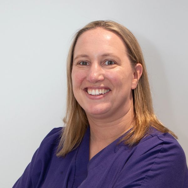 Anna Marie, a veterinary surgeon standing arms folded, purple scrub top. smiling