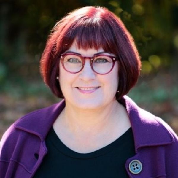 Woman with red hair and glasses smiling.