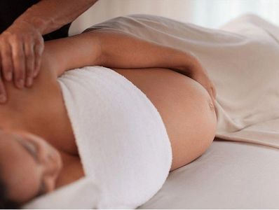 Pregnant woman receiving a gentle shoulder massage while lying down.