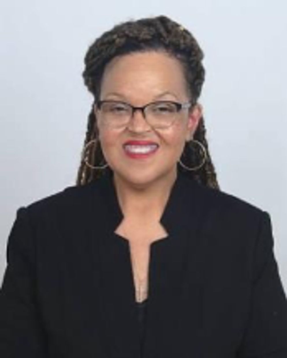 Woman with glasses and braided hair smiling, wearing a black blazer.