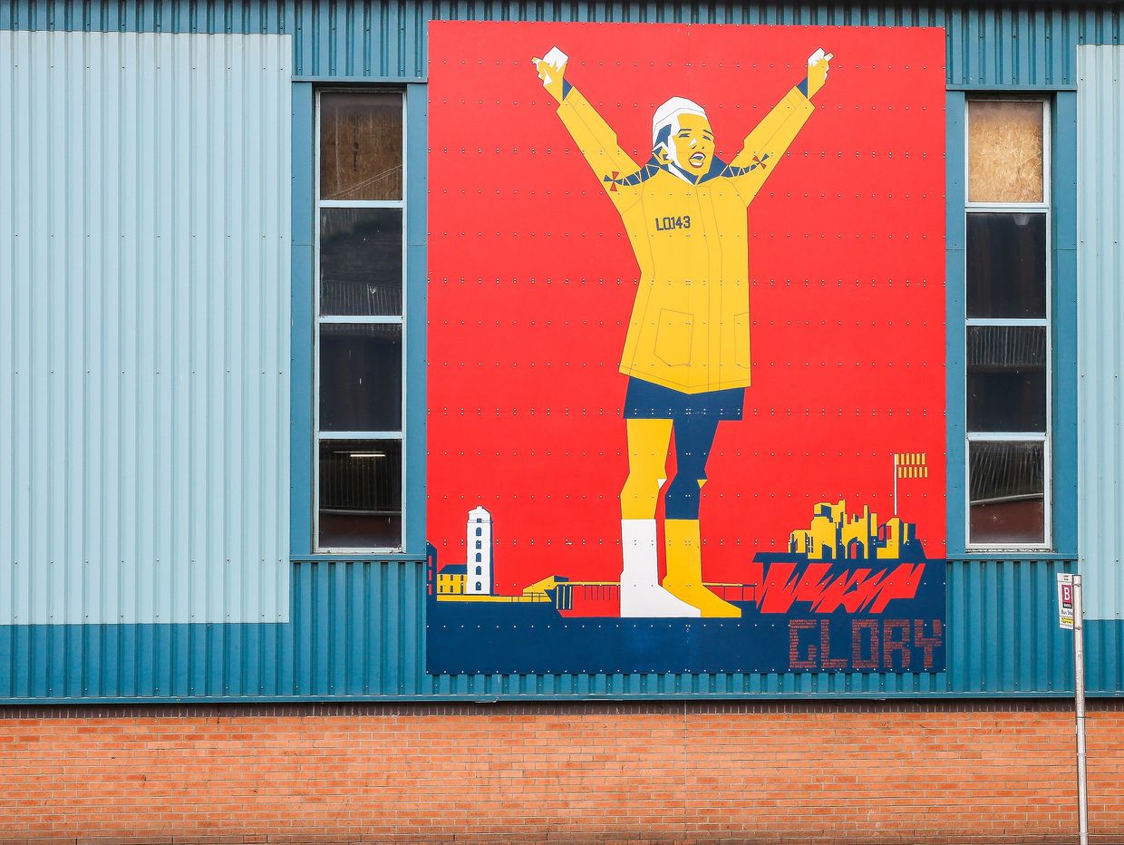 Colorful mural of a person in yellow with raised arms on a red background.