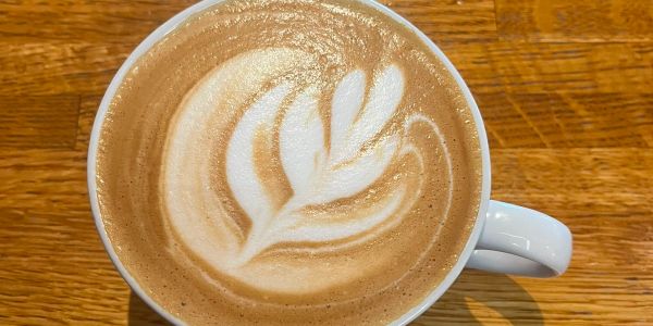A cup of latte with leaf-shaped latte art on wooden table.