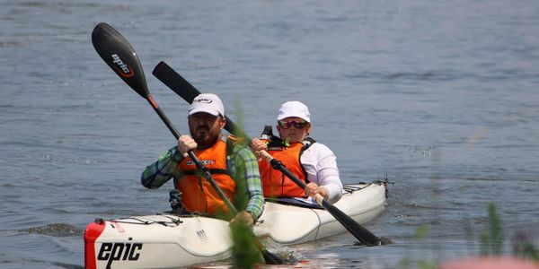 Two people kayaking on calm water wearing orange life vests.