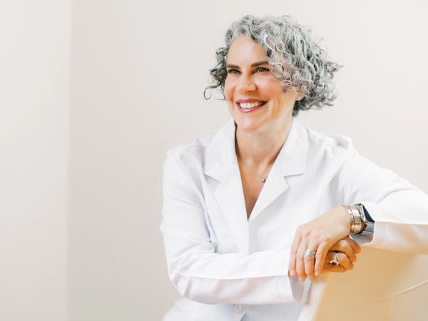 Smiling woman in white coat with curly gray hair.