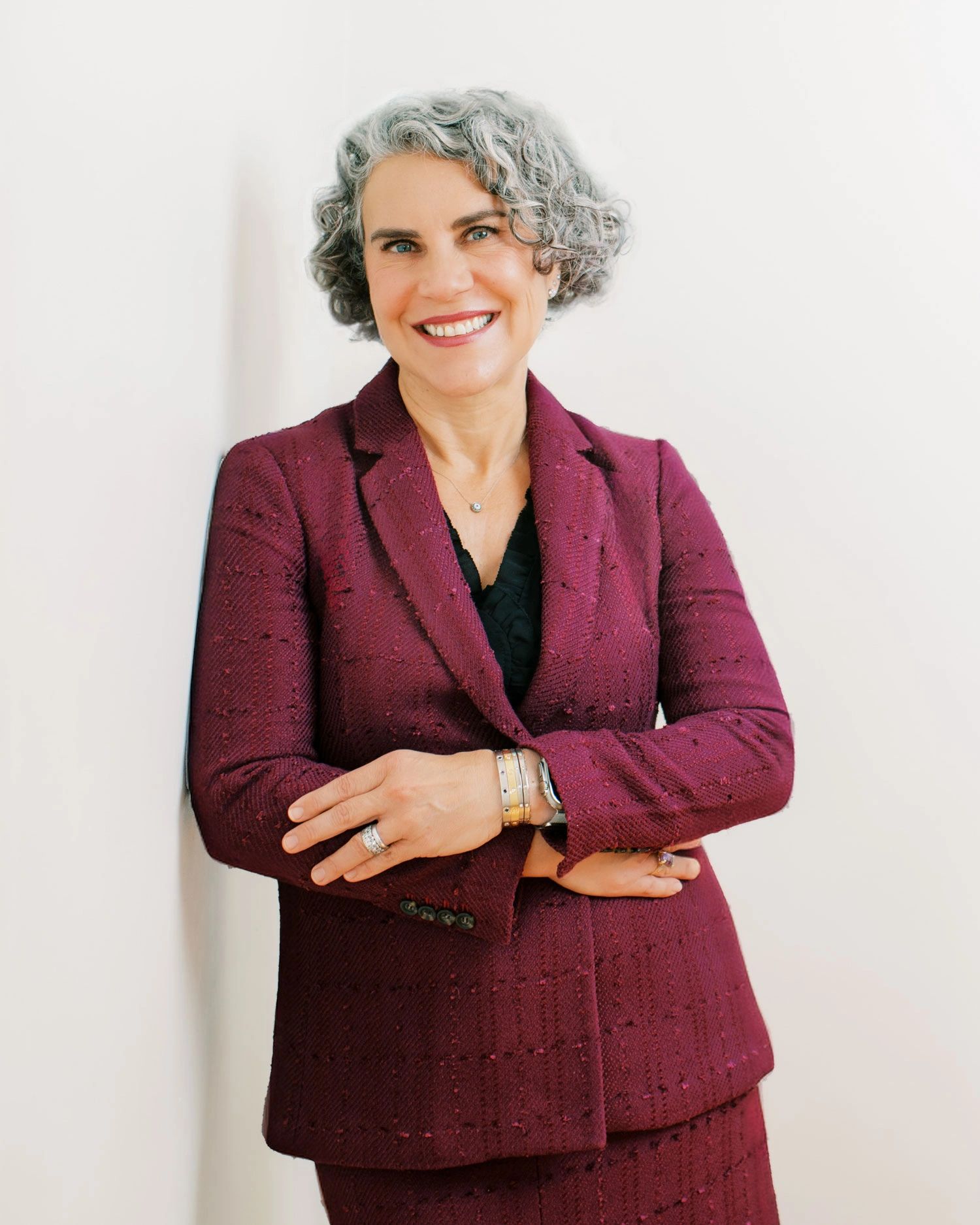 Smiling woman with gray curly hair wearing a maroon suit.