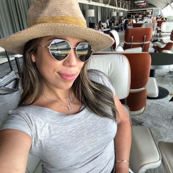 Woman in a straw hat and heart-shaped sunglasses smiling indoors.
