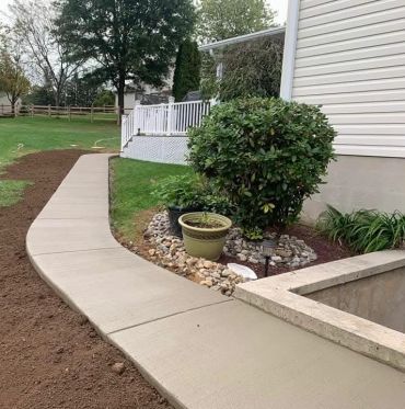 Newly poured concrete sidewalk next to a garden and house.