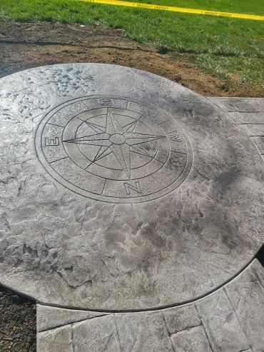 Concrete compass design etched into a circular slab outdoors.