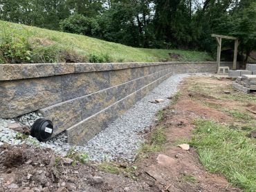 Newly built stone retaining wall with gravel base in a backyard.