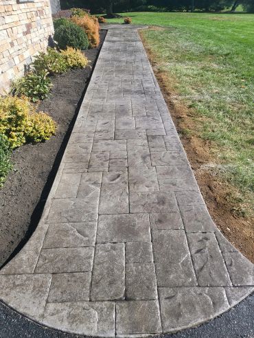 Stamped concrete walkway with a stone pattern next to a garden and lawn.
