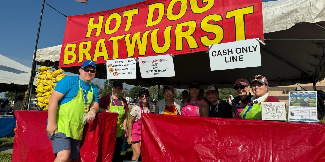 Group of people smiling at a hot dog and bratwurst stand with a cash-only sign.