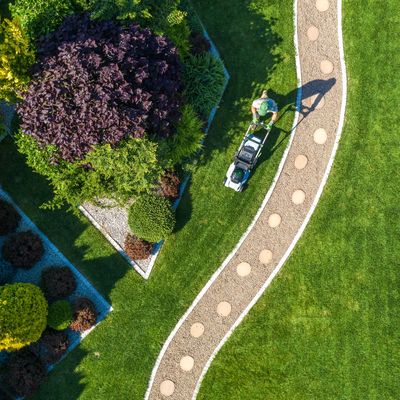 Aerial view of a person mowing a well-manicured lawn with a lawnmower beside a curved gravel path.