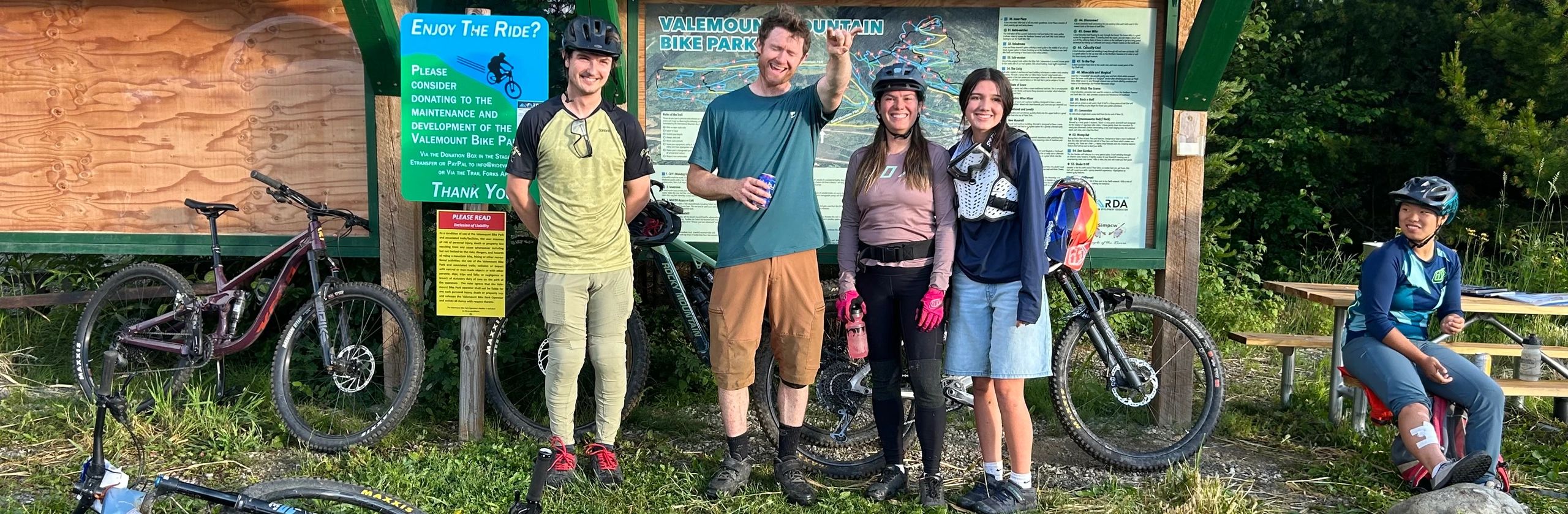 Group of mountain bikers posing happily in front of trail information boards.
