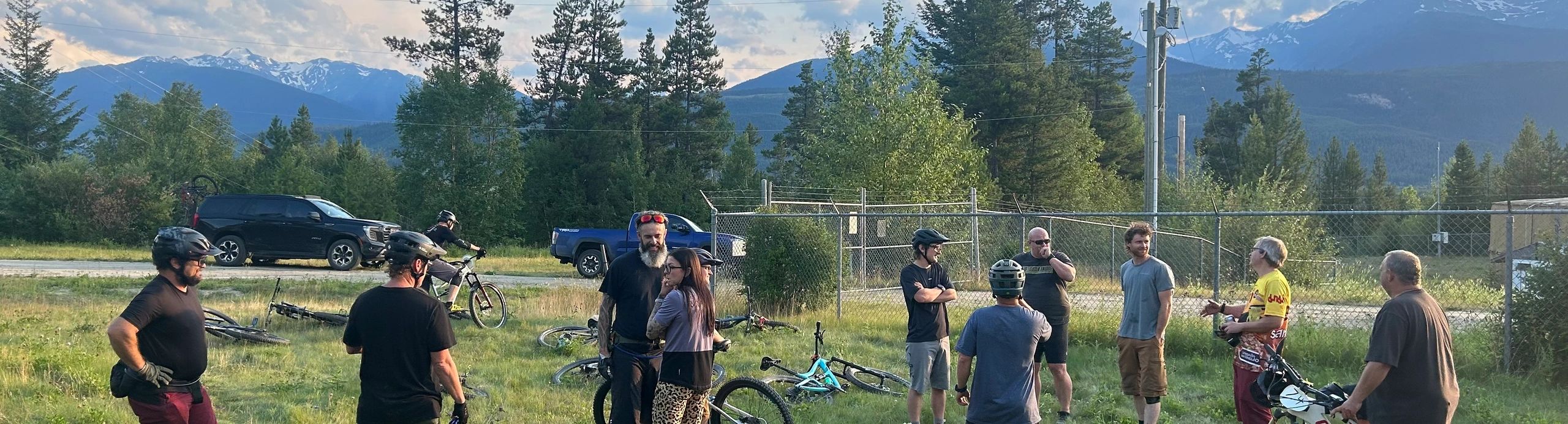 Group of people with bikes in a grassy area by mountains.