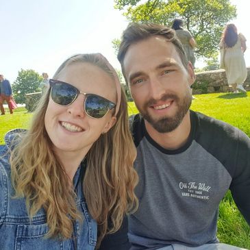 A smiling couple takes a selfie outdoors on a sunny day.
