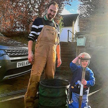 Man and child stand next to a barrel outdoors on a sunny day.