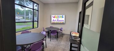 A small art room with purple chairs and round tables.
