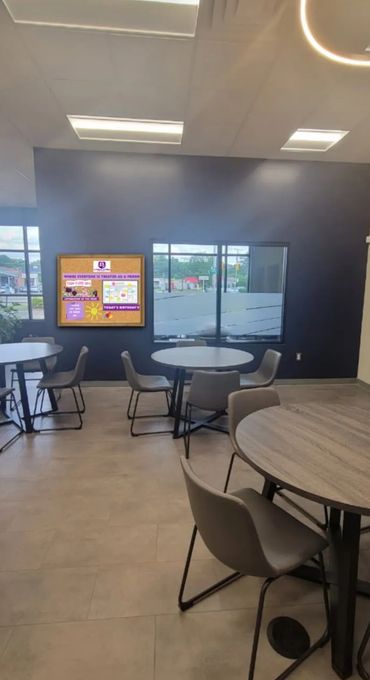 Modern break room with round tables and chairs, featuring a bulletin board on a dark wall.