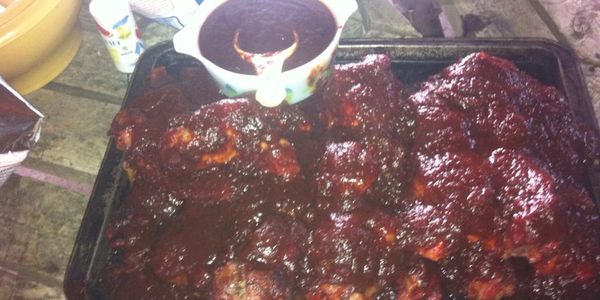 Tray of ribs covered in barbecue sauce with extra sauce in a bowl.