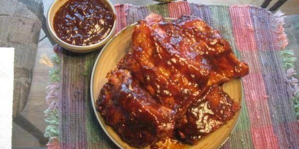 A plate of barbecued ribs with a bowl of extra barbecue sauce.