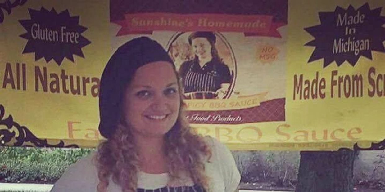Smiling woman in apron at a booth for gluten-free, all-natural BBQ sauce.