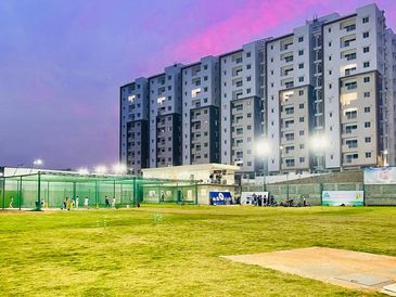 Residential buildings near a well-lit cricket ground at dusk.