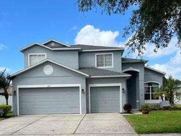 Two story grey stucco home with 3 car garage, mature landscaping and a small covered front porch.