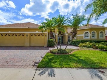 One story yellow stucco home with red paver driveway, palm trees and glass double font doors.