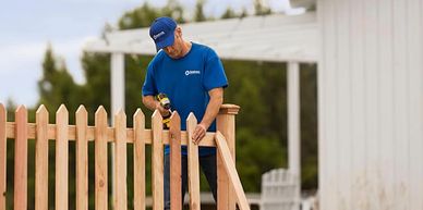 Man in blue shirt assembling a wooden fence with a power drill.