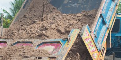 A blue dump truck unloading a large pile of dirt outdoors.