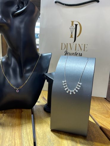 Elegant necklaces displayed on black and gray stands with Divine Jewelers bag in background.