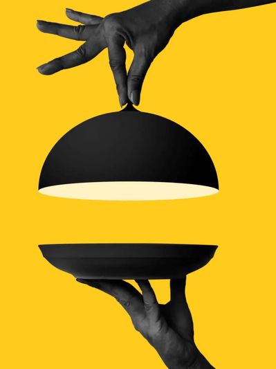 Hands presenting an empty black serving dish against a yellow background.