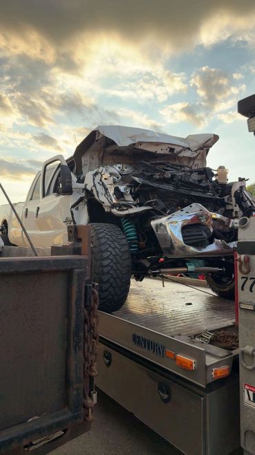 White pickup truck with severe front-end damage on a flatbed tow truck.