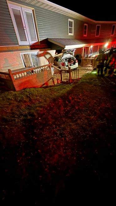 Car crashed into a house porch at night with emergency responders present.