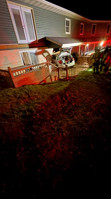 Car crashed into a house porch at night with emergency responders present.