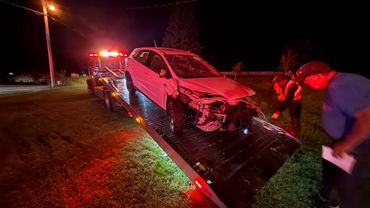Damaged white car being loaded onto a tow truck at night.