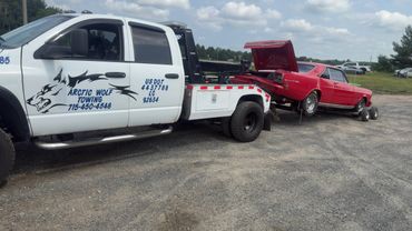 White Arctic Wolf Towing truck towing a red vintage Blaze 350 car.