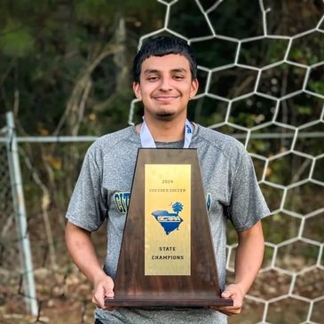 Young soccer player proudly holding a 2024 state champions trophy.
