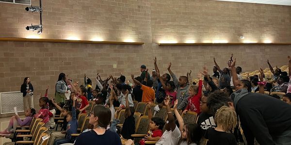 Children eagerly raising hands in a school auditorium.