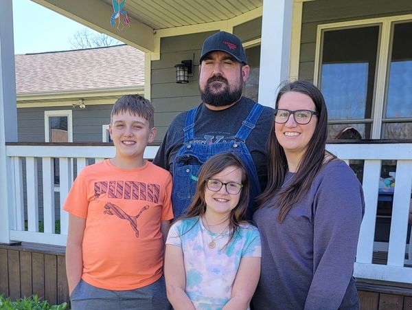Happy family of four posing outside their home.