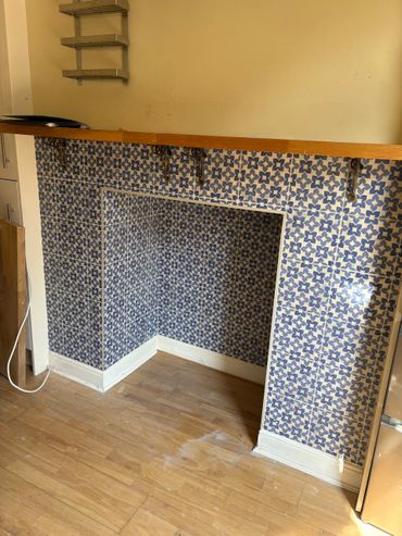 A tiled fireplace alcove with blue floral pattern and wooden floor.
