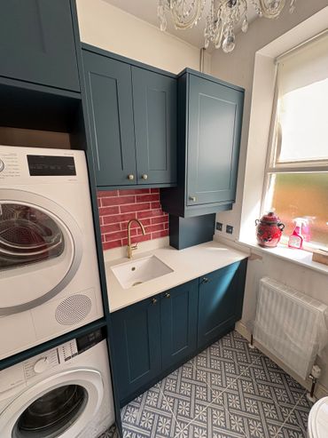 Compact laundry room with teal cabinets, white countertop, and patterned floor tiles.