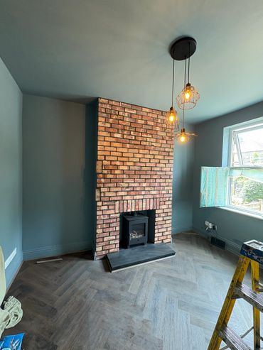 Cozy room with brick fireplace, industrial pendant lights, and herringbone wooden floor.
