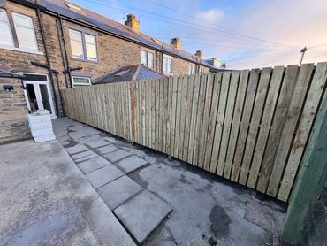 Newly installed wooden fence with stone pathway beside a brick house.