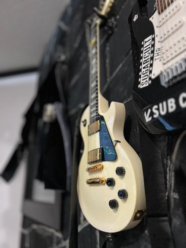 Cream-colored electric guitar hanging on a wall with a black guitar beside it.