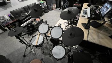 Electronic drum kit set up in a music studio with various instruments and equipment.
