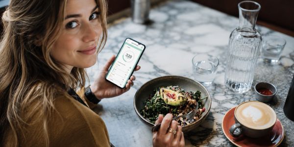 Woman tracking calories on her phone while eating a healthy meal at a cafe.