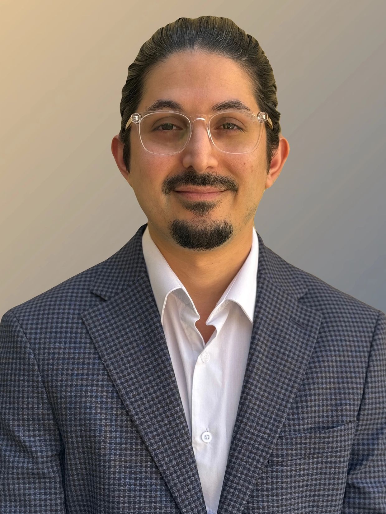 A man in glasses wearing a checkered suit and white shirt, smiling softly.