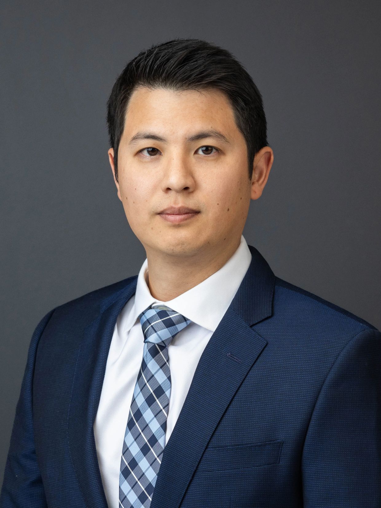 Professional man in a blue suit and checkered tie against a gray background.