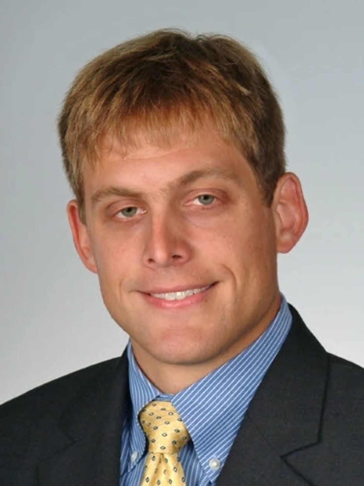 A man in a suit smiling slightly for a portrait.